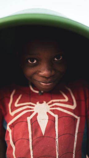 A vertical shot of young African boy in Mozambique holding a green bowl on his head to net water from River