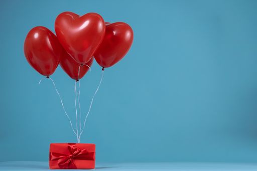 A heart-shaped red allons attached to a wrapped gift with a red ribbon on a blue background