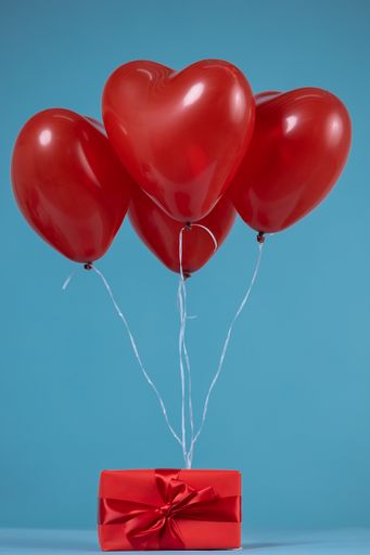 A heart-shaped red balloons attached to a wrapped gift with a red ribbon on a blue background