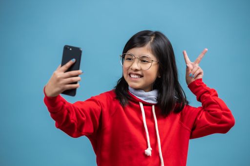 A Hispanic female child taking a selfie with a peace sign