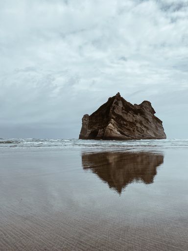 A vertical shot of big rock with its reflection on the seawater