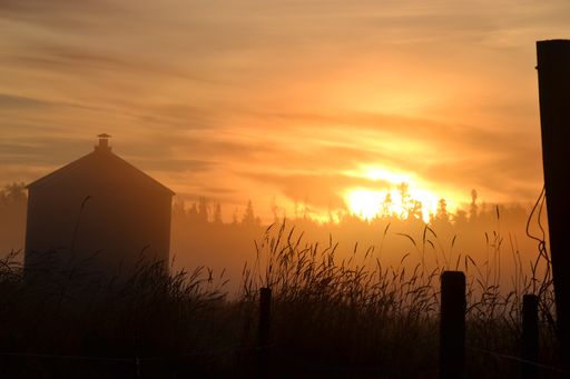 A silhouette shot of a small house with chimney in the field during a beautiful golden sunset
