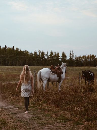 A rear view of a blonde woman walking near the horses in the field