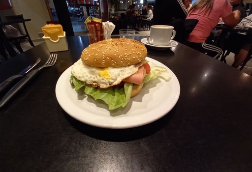 high angle shot of a complete hamburger or ground meat burger with egg, tomato and lettuce in a white plate on a dark wooden table