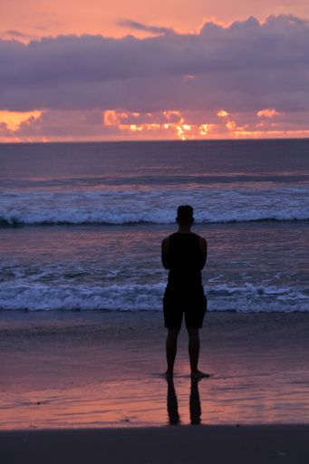 a vertical shot of a male shot from behind on the background of the large waves at the red sunset
