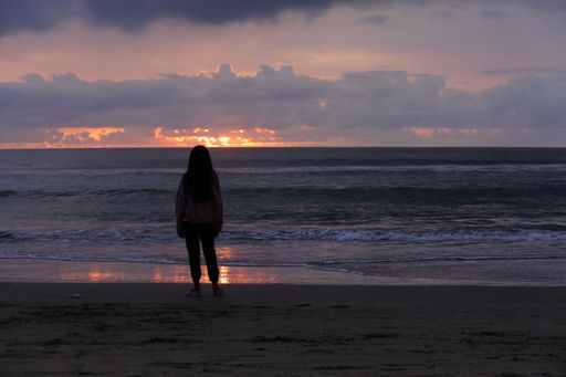 a female shot from behind on background of dark low waves at sunrise