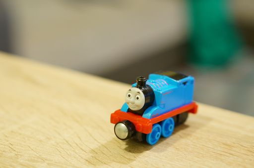 Blue Thomas and Friends blue toy locomotive standing on a wooden table in soft focus background.