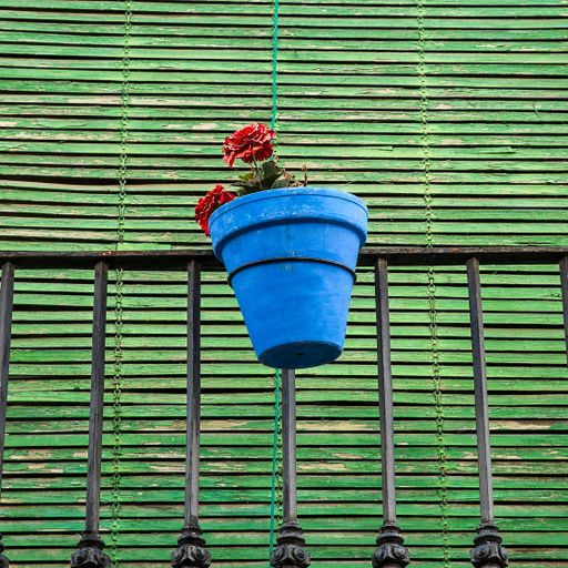 A low angle shot of red flowers in a blue pot attached to a balcony railing with a green background