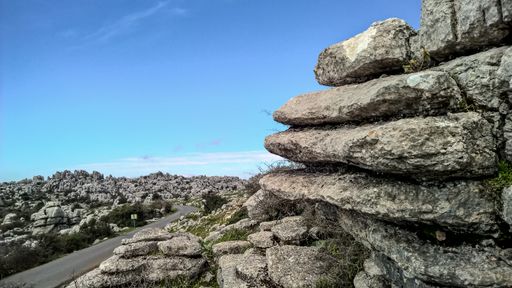 A wide shot of layers of rocks and a clear bright sky along a smooth asphalt road