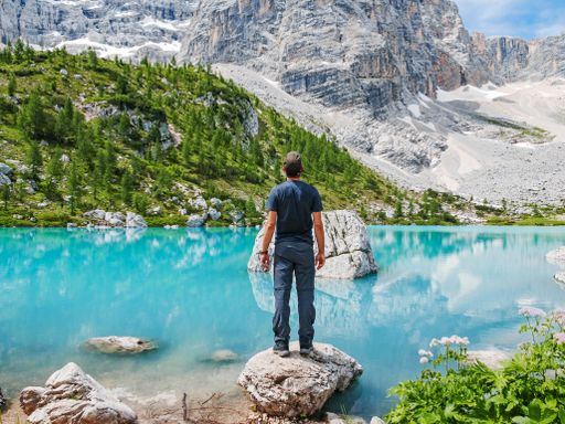 A person standing on a rock near a crystal clear lake under the sunlight
