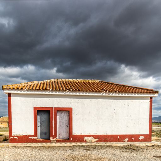 A white building with red frames on its corners under a sky full of clouds