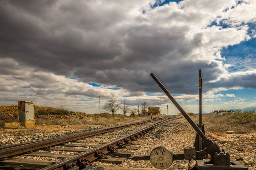 A wide angle shot of train tracks going over a dry field under a sky full of clouds