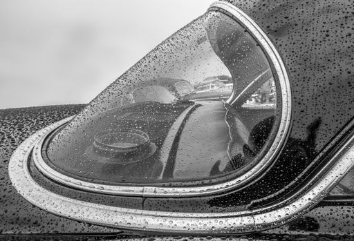 A grayscale shot of the front part of a car covered in raindrops