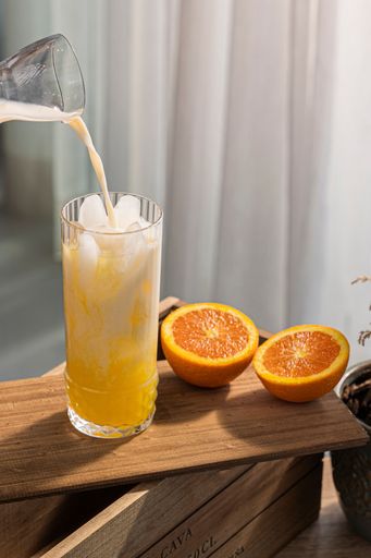 An image of a pitcher pouring milk over a glass of iced orange juice