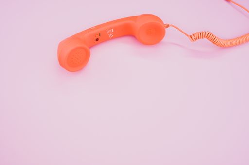 A high angle shot of a vintage orange telephone on a pink surface