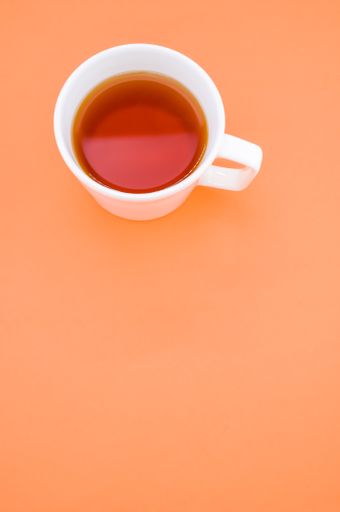 A vertical high angle shot of a cup of tea on an orange surface