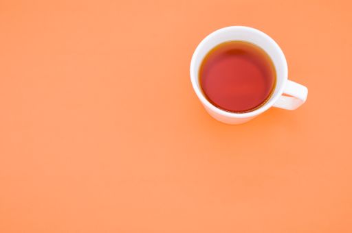 A high angle shot of a cup of tea on an orange surface