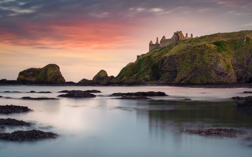 A majestic castle standing proudly on a rocky coast at sunset