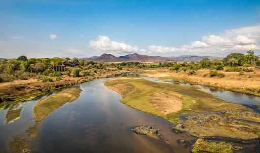 A wide angle shot of a small lake surrounded by mountains and greenery during daytime
