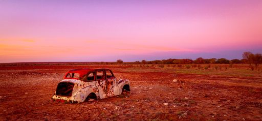 An image of an old, rusty, and abandoned vintage car in the middle of a desert landscape