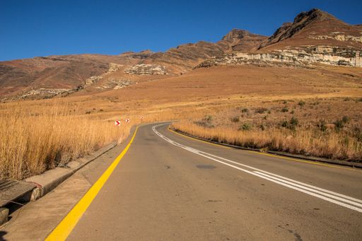 A wide angle shot of a road going on a mountain surrounded by bushes and dry grass