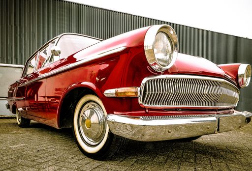 A low angle shot of a red car standing in front of a grey garage during daytime
