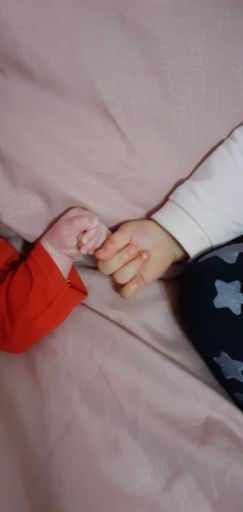 A vertical shot of a baby holding a hand of a newborn baby on a pink background
