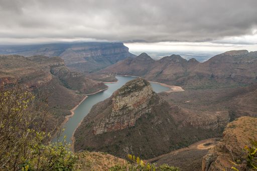 A wide angle shot of a small lake surrounded by mountains and greenery during daytime