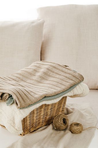 A vertical shot of a gray sofa with a basket of folded clothes on a small table near it
