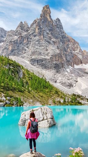 A vertical shot of a female with a backpack standing on a stone near a crystal clear