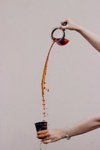 A vertical shot of a female pouring coffee from a kettle to a cup on a grey background