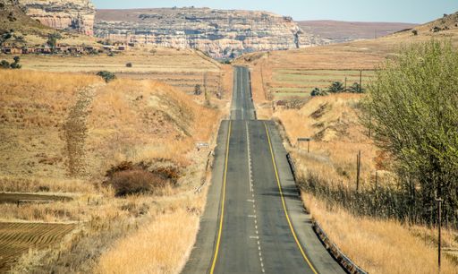 A wide angle shot of a road going on a mountain surrounded by bushes and dry grass