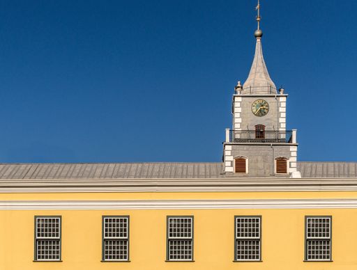 A closeup shot of the roof of a building with a small tower and a clock under a cloudy sky
