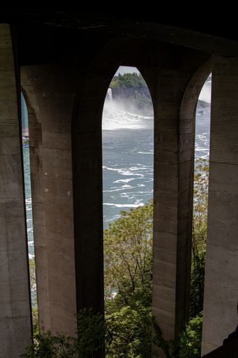 A vertical shot where stone arcs cover a view of the river where a waterfall falls