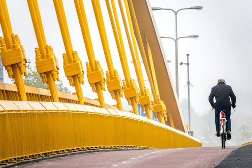A man dressed in black riding a bicycle next to a wall made of yellow metal