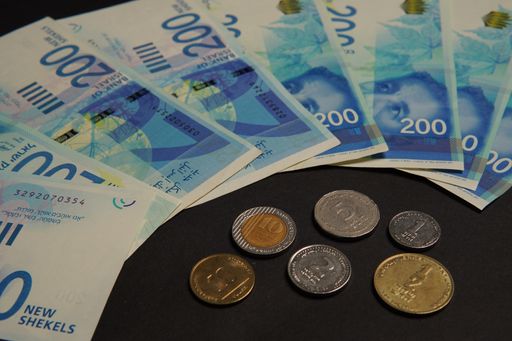 A flat lay of Israeli banknotes and coins on a black surface - finance, savings concept
