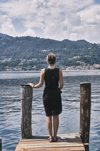 A vertical shot of a female standing on a viewing deck at the Lake Orta in Orta San Giulio, Italy