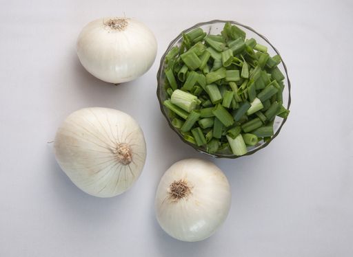 A top view of fresh raw white onions and chopped green onions in a bowl on a white background