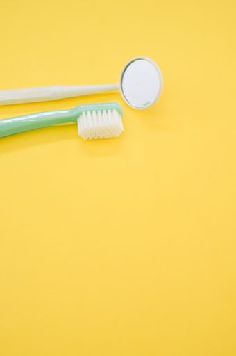 A vertical shot of a toothbrush and dental mouth mirror isolated on yellow background for a copy space