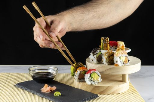 A closeup of a male hand holding chopsticks and picking up a sushi roll from a wooden tray