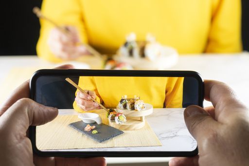 A selective closeup of a phone taking a photo of a person eating sushi