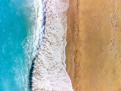 An aerial view of ocean waves crashing on a sandy beach