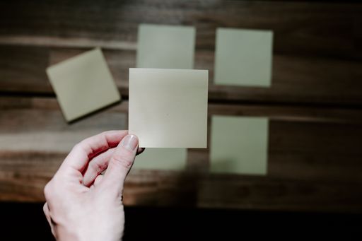 A top view of a person holding a sticky note paper against the others attached on a wooden table