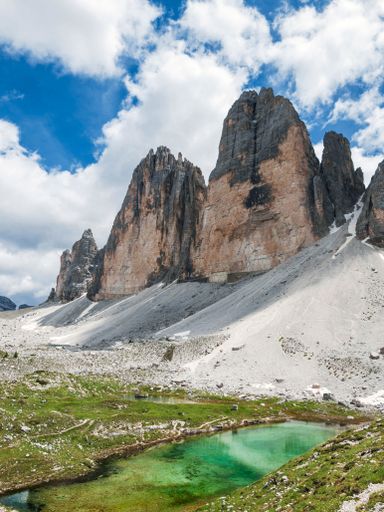 A vertical shot of a lake by the beautiful mountain peaks captured on a sunny day
