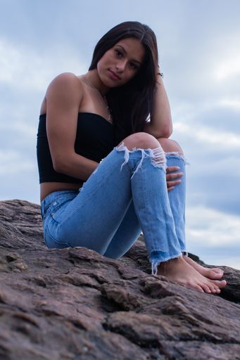 A vertical shot of a beautiful young Hispanic female with long hair sitting on rocks