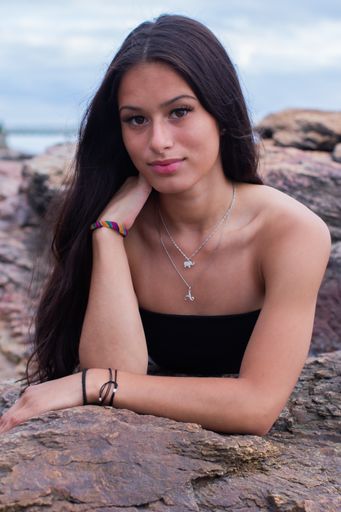A vertical shot of an attractive Hispanic female wearing a strapless crop top lying on rocks