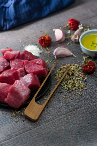 A vertical shot of raw cut meat, garlic cloves, dried pepper, oil on the table - making dinner