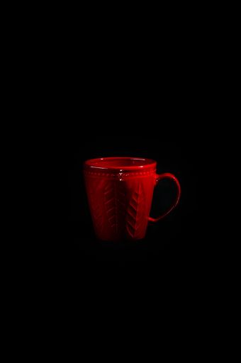 A closeup view of an empty red mug with leave on it isolated on a black background