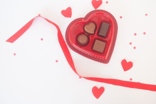A top view of a heart-shaped box of Bonbonniere and other decorations on a white surface