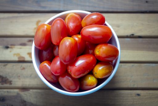 A top view of porcelain bowl with cherry tomatoes on wooden table
